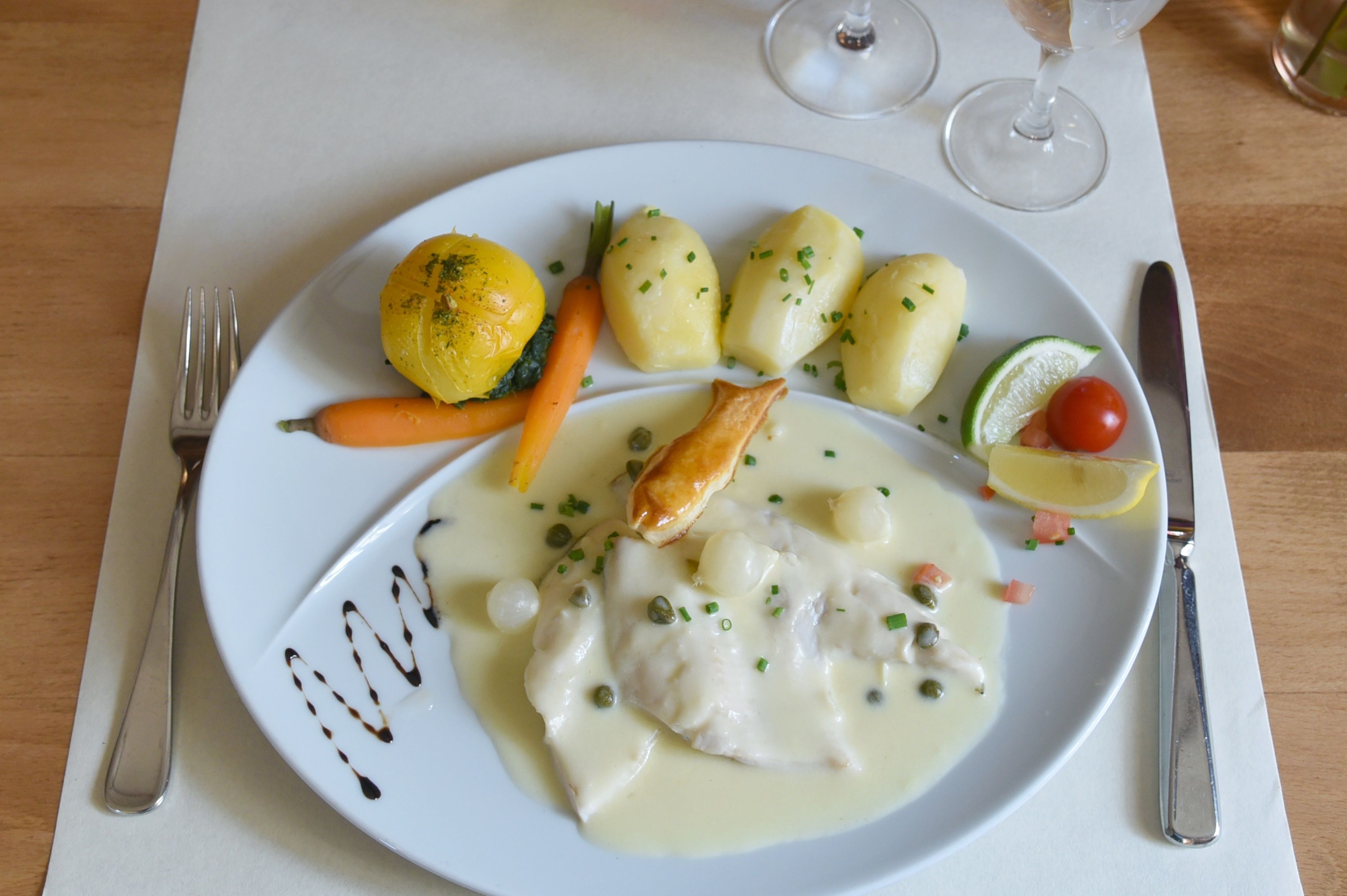 Une assiette de nourriture comprenant du poisson, des pommes de terre, des carottes et une tranche de citron.