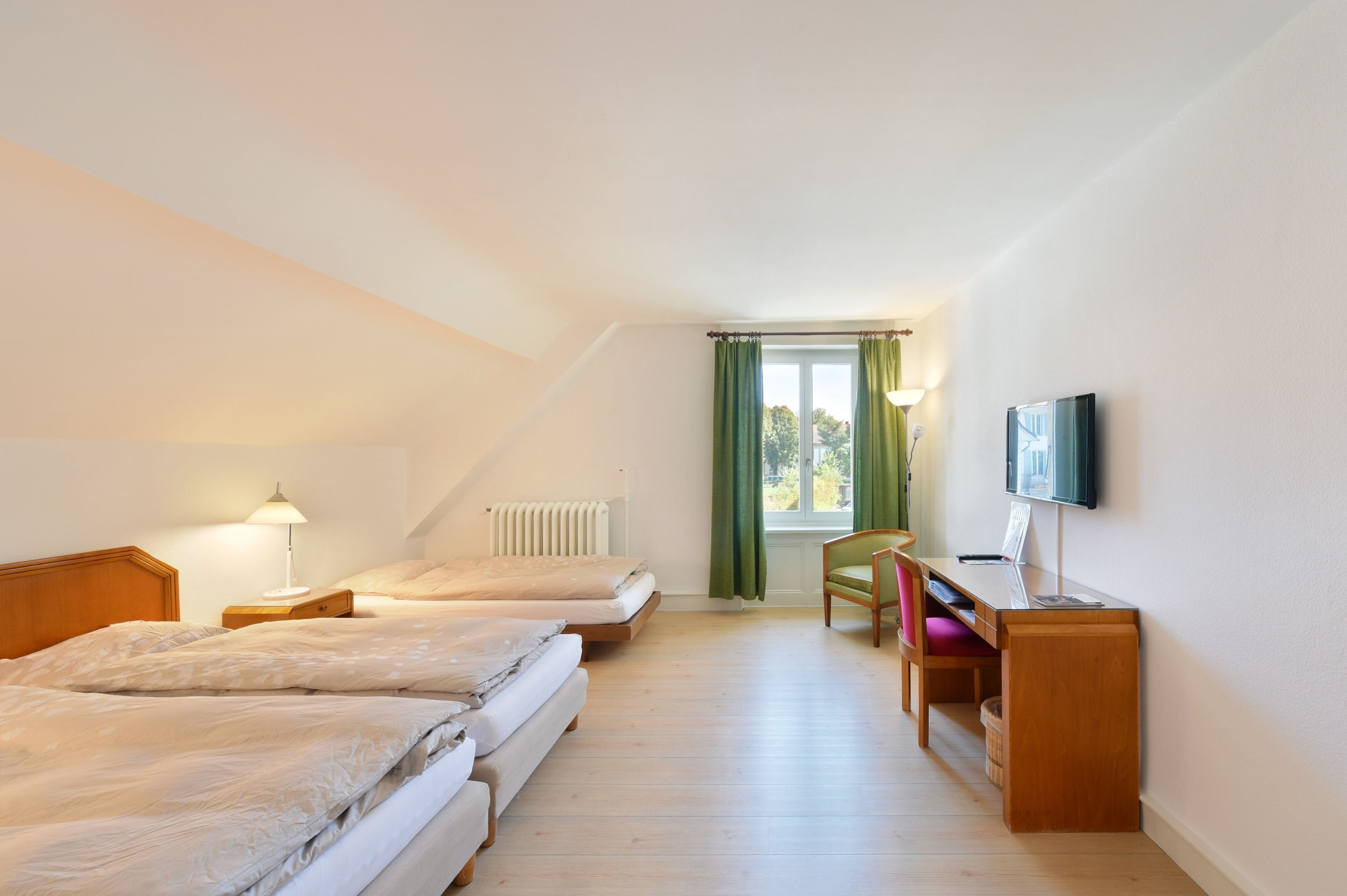 Une chambre avec deux lits, un bureau, une chaise, une télévision et une fenêtre avec des rideaux.