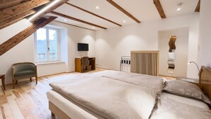 A bedroom with a large bed, wooden beams, a desk, a chair, a TV, and a window with a view. - Hôtel de l'Aigle (Val-de-Travers)
