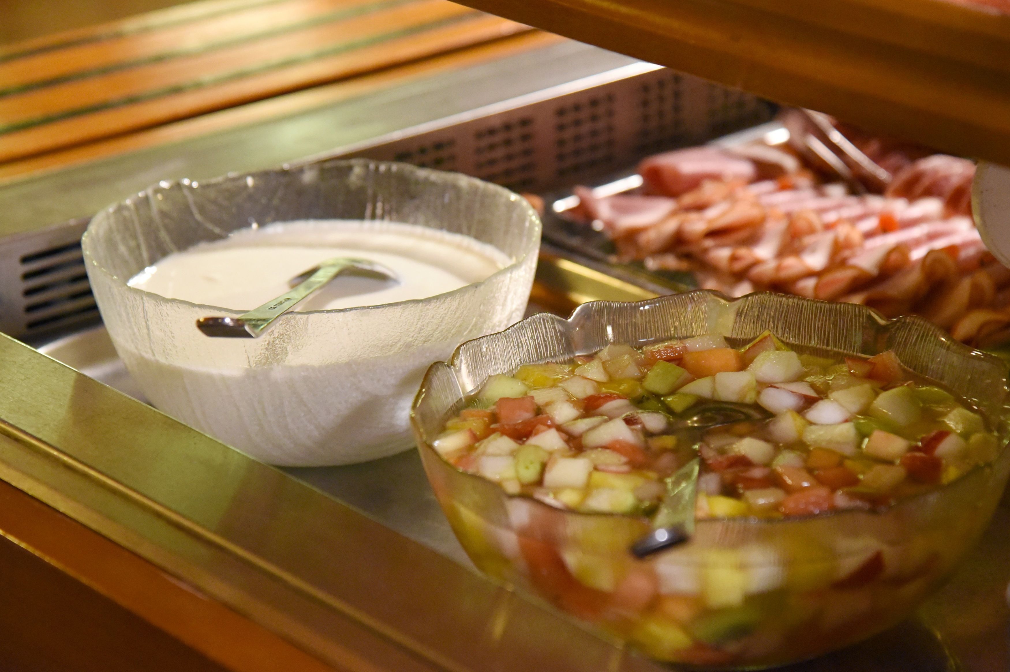 A buffet with various food items including a bowl of creamy dip, a bowl of diced vegetables, and sliced meats.