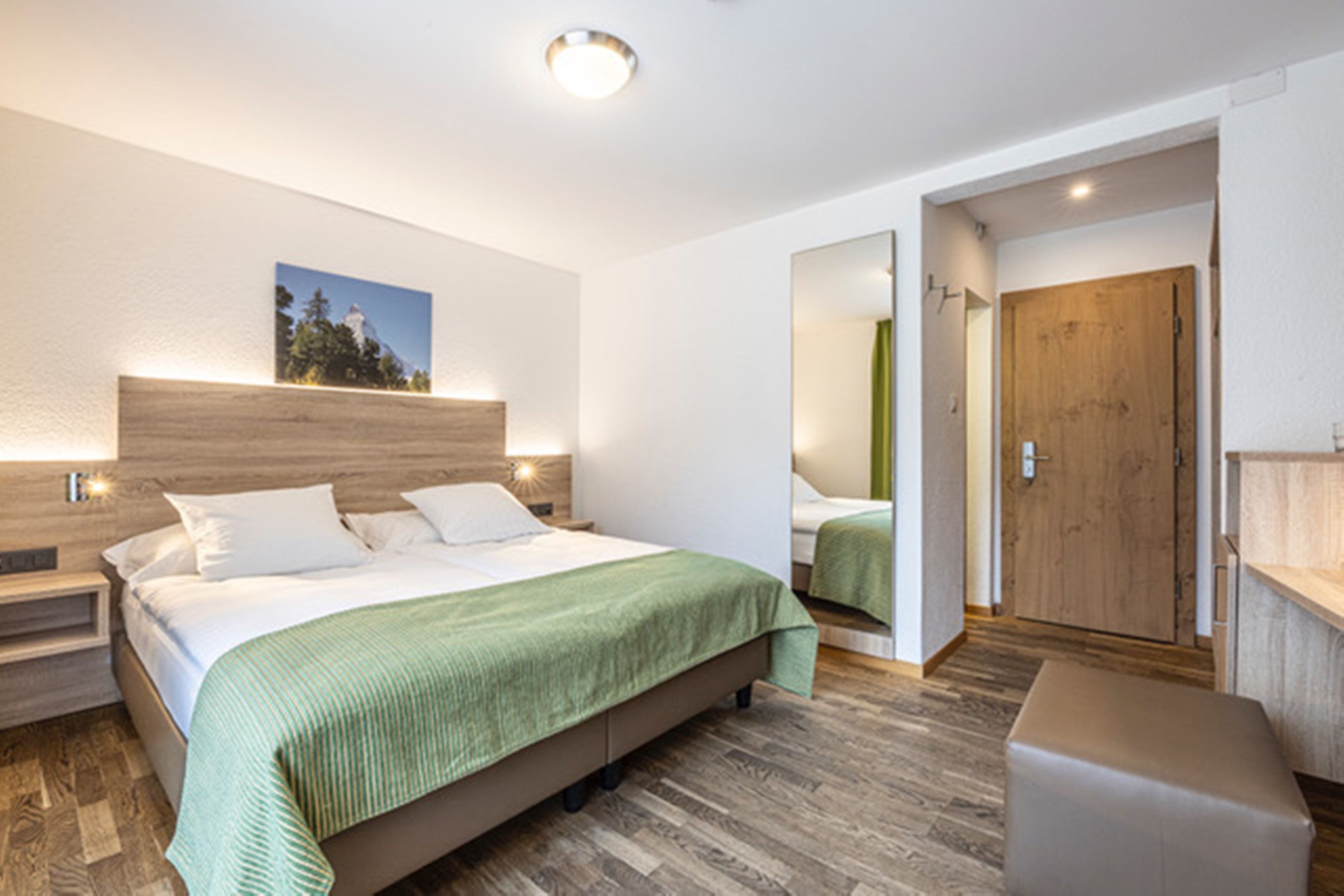 A modern bedroom with a wooden headboard, a green bedspread, and a nightstand with a lamp.