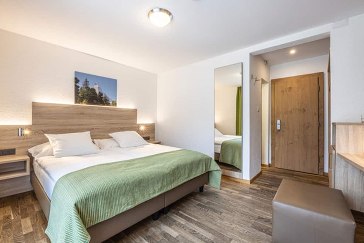 A modern bedroom with a wooden headboard, a green bedspread, and a nightstand with a lamp.