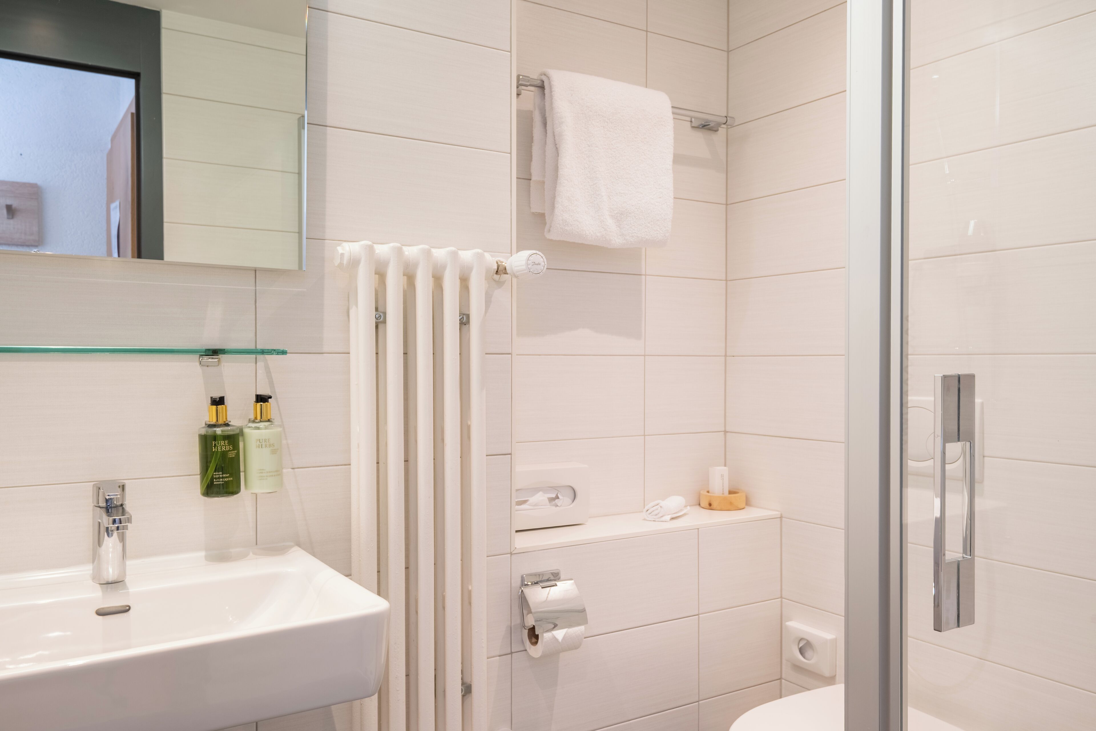 A modern bathroom with a white sink, a glass shower enclosure, and a towel rack.