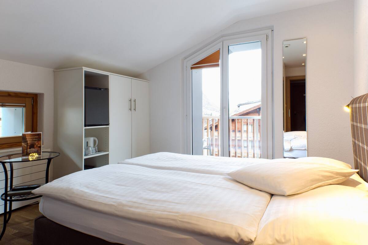 A hotel room with a bed, a desk, a wardrobe, and a balcony with a view.
