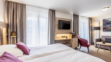 A hotel room with two beds, a desk, a TV, a chair, and a sofa.
