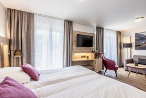 A hotel room with two beds, a desk, a TV, a chair, and a sofa.