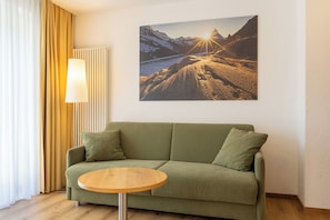 A green sofa with a round wooden table in front, a lamp, and a mountain landscape painting on the wall. - Hotel Bristol (Zermatt)