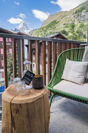 A balcony with a wooden table, a wicker chair, and a view of a mountain. - Hotel Bristol (Zermatt)