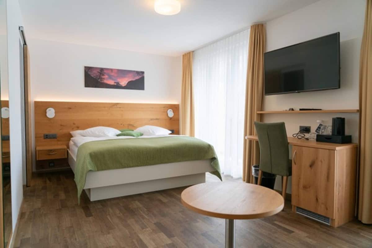 A hotel room with a bed, a desk, a chair, a television, and a painting on the wall.