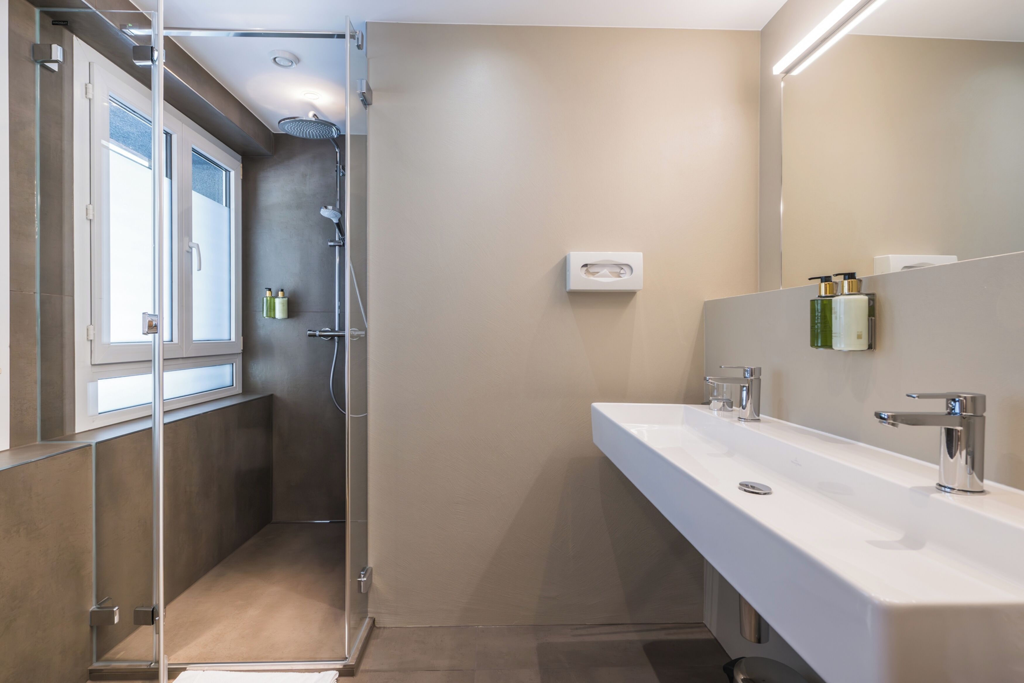 Ein modernes Badezimmer mit einer Duschkabine aus Glas, einem großen Spiegel und einer weißen Ablagefläche mit Waschbecken und Armatur.