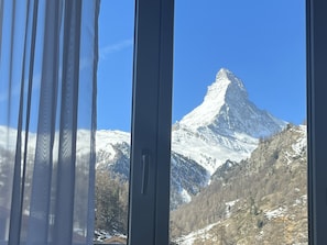 A mountain view through a window with curtains, featuring a snow-covered peak. - Hotel Bristol (Zermatt)