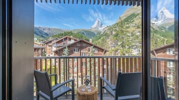 Un balcón con sillas de mimbre y una mesa de madera, con vista a una montaña y su cima destacada.