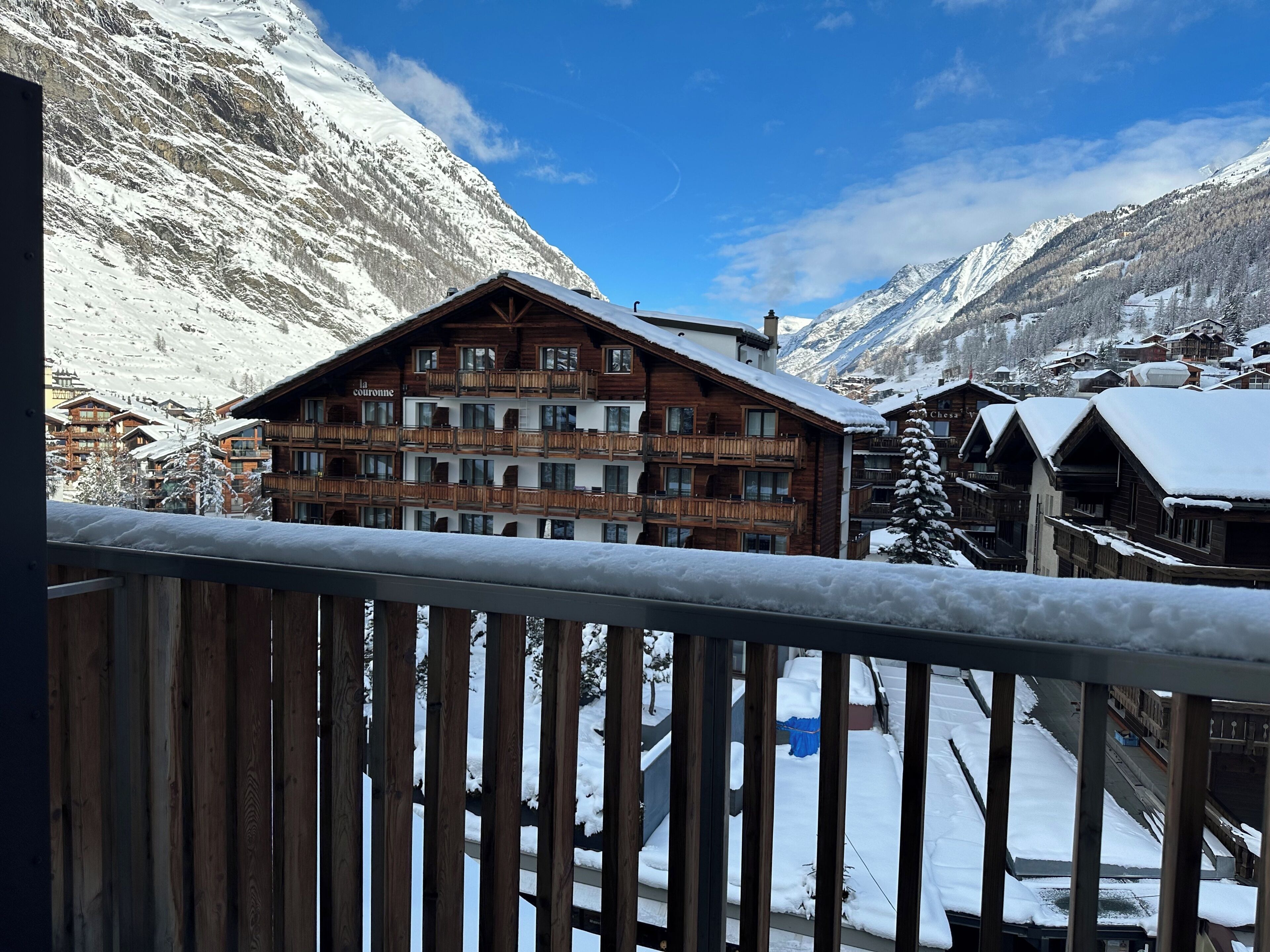 Un bâtiment de style chalet en bois, doté de nombreux balcons, entouré de montagnes enneigées et surplombant un ciel dégagé.