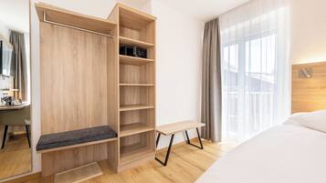 Una camera d'albergo moderna con un armadio in legno, un comodino, un letto e un'ampia finestra con tende.