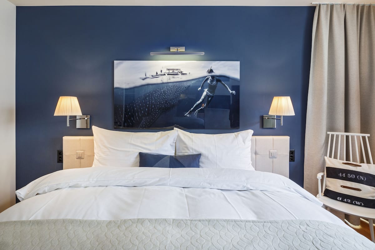 A hotel room with a large bed, two bedside lamps, a wall-mounted TV, and a chair with a luggage tag.