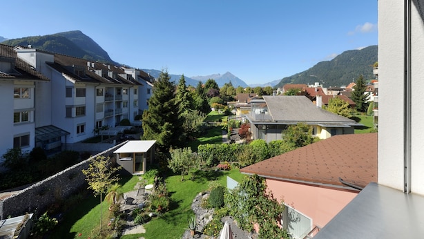 A residential area with a view of mountains, featuring houses with sloped roofs, a stone wall, and a well-maintained garden. - Hotel Derby Interlaken - Action & Relax Hub (Interlaken)
