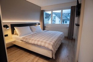 Un dormitorio con cama, mesitas de noche, una ventana con cortinas y vistas a edificios.