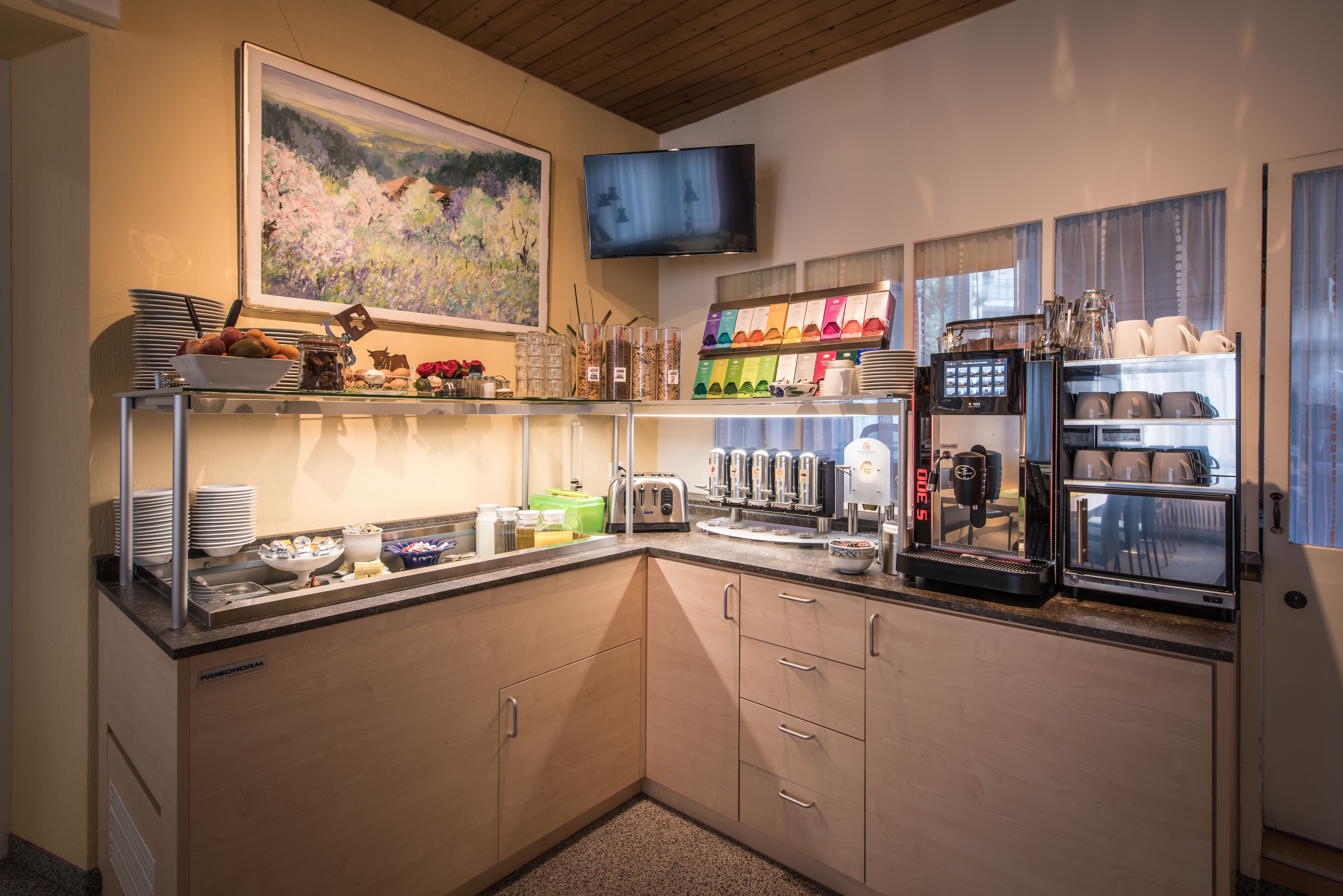 Un comptoir pour le petit-déjeuner avec divers aliments, une machine à café et un téléviseur fixé au mur.