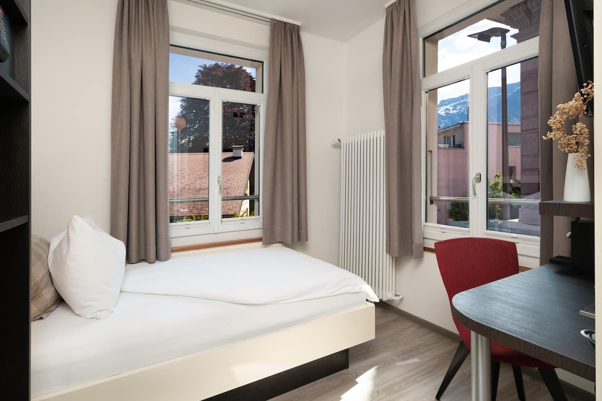 A modern bedroom with a bed, a red chair, a table, and a window with curtains.
