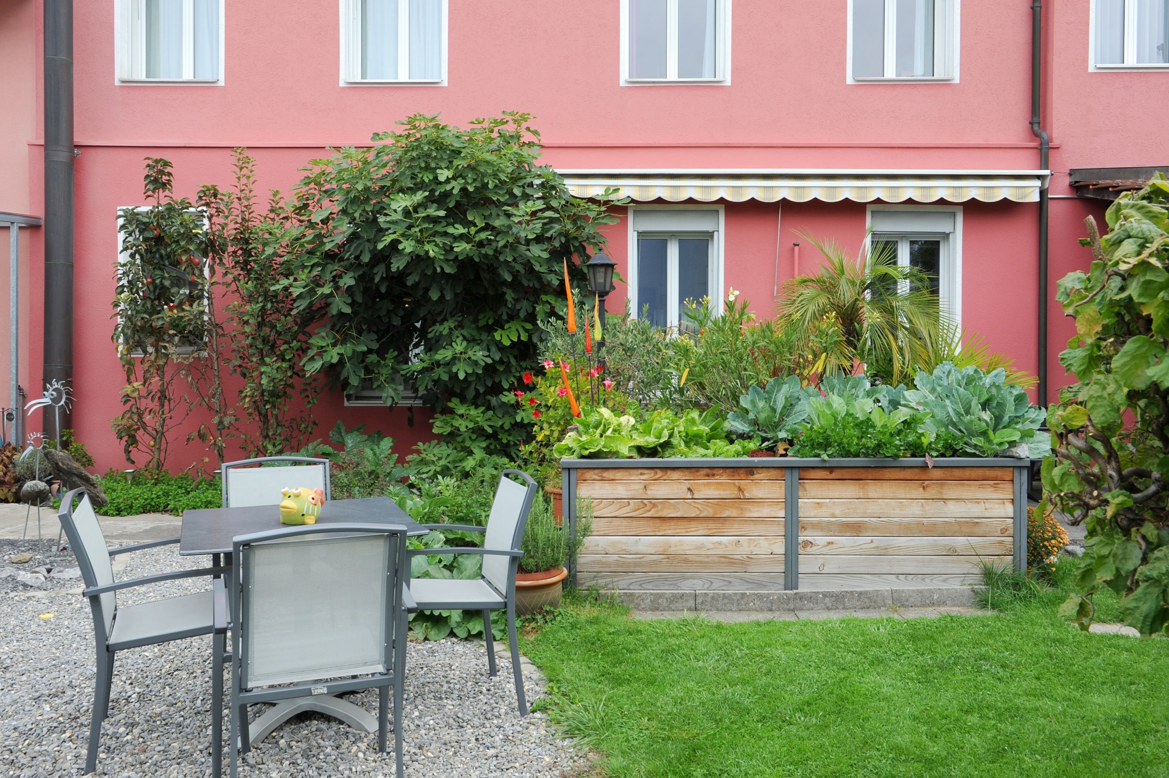 A red building with a garden, a wooden bench, and a table with chairs.
