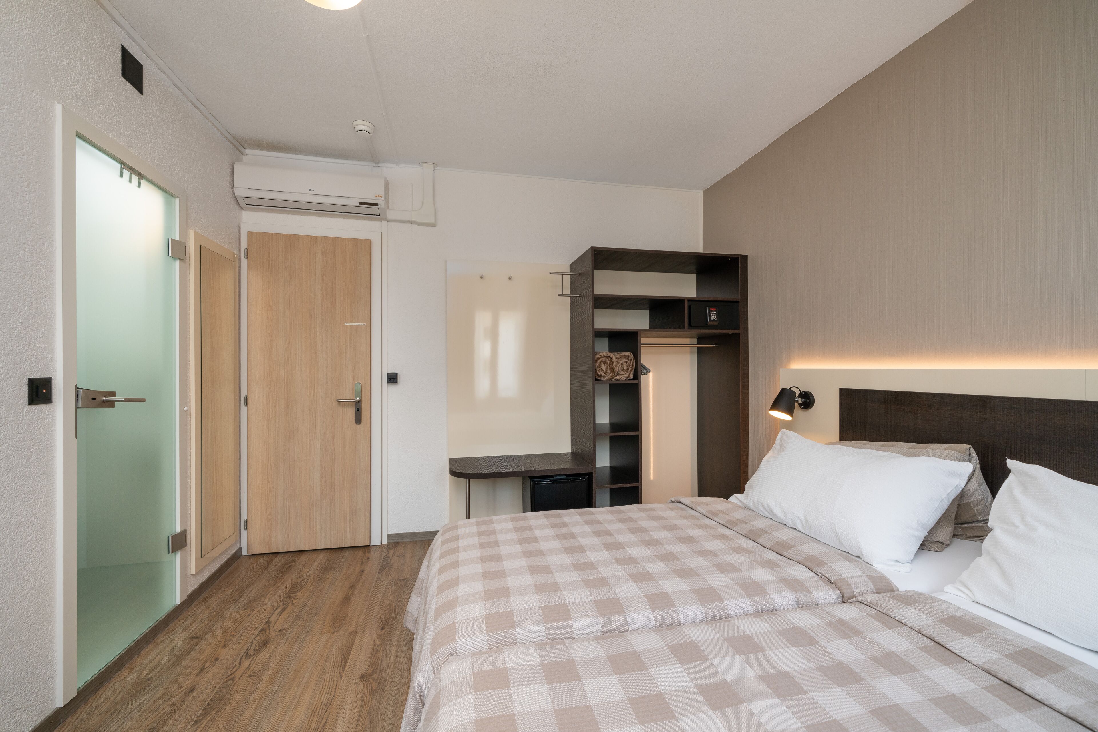 Habitación de hotel con edredón a cuadros, una puerta de madera, un escritorio pequeño y un armario empotrado.