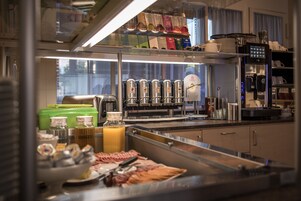 Zona de bufé con diferentes opciones de comida, una máquina de café y un dispensador de jugo.