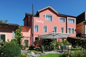 Un edificio con el nombre 'Derby' en su fachada, que cuenta con un patio con asientos exteriores y un gran paraguas.
