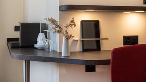 A modern hotel room with a dark wooden desk, a white vase with dried flowers, a glass carafe, a black speaker, and a red chair. - Hotel Derby Interlaken - Action & Relax Hub (Interlaken)