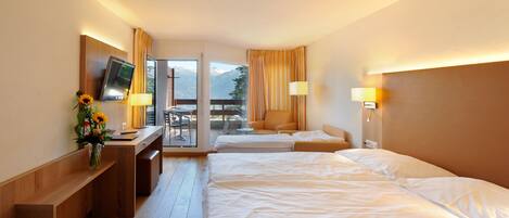 Habitación de hotel con dos camas, un escritorio y televisión, y vistas a montañas a través de la ventana.