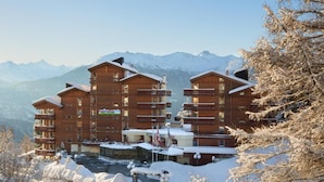 A multi-story wooden lodge with balconies, a restaurant/bar, and a view of snow-covered mountains. - Hotel Helvetia Intergolf (Crans-Montana)