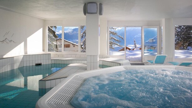 A modern indoor swimming pool with a hot tub, large windows with snowy mountain views, and a clean, white interior. - Hotel Helvetia Intergolf (Crans-Montana)
