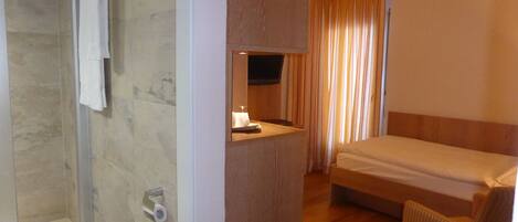 A hotel room with a shower, a bed, a wooden panel, and a television.