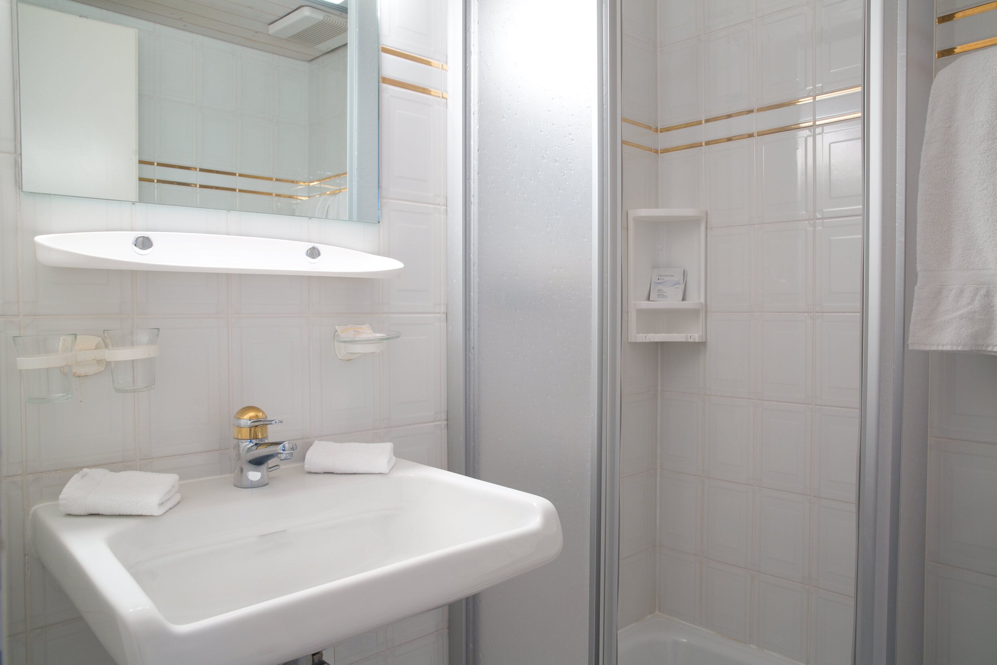 Une salle de bain avec un lavabo blanc, un miroir et une cabine de douche.