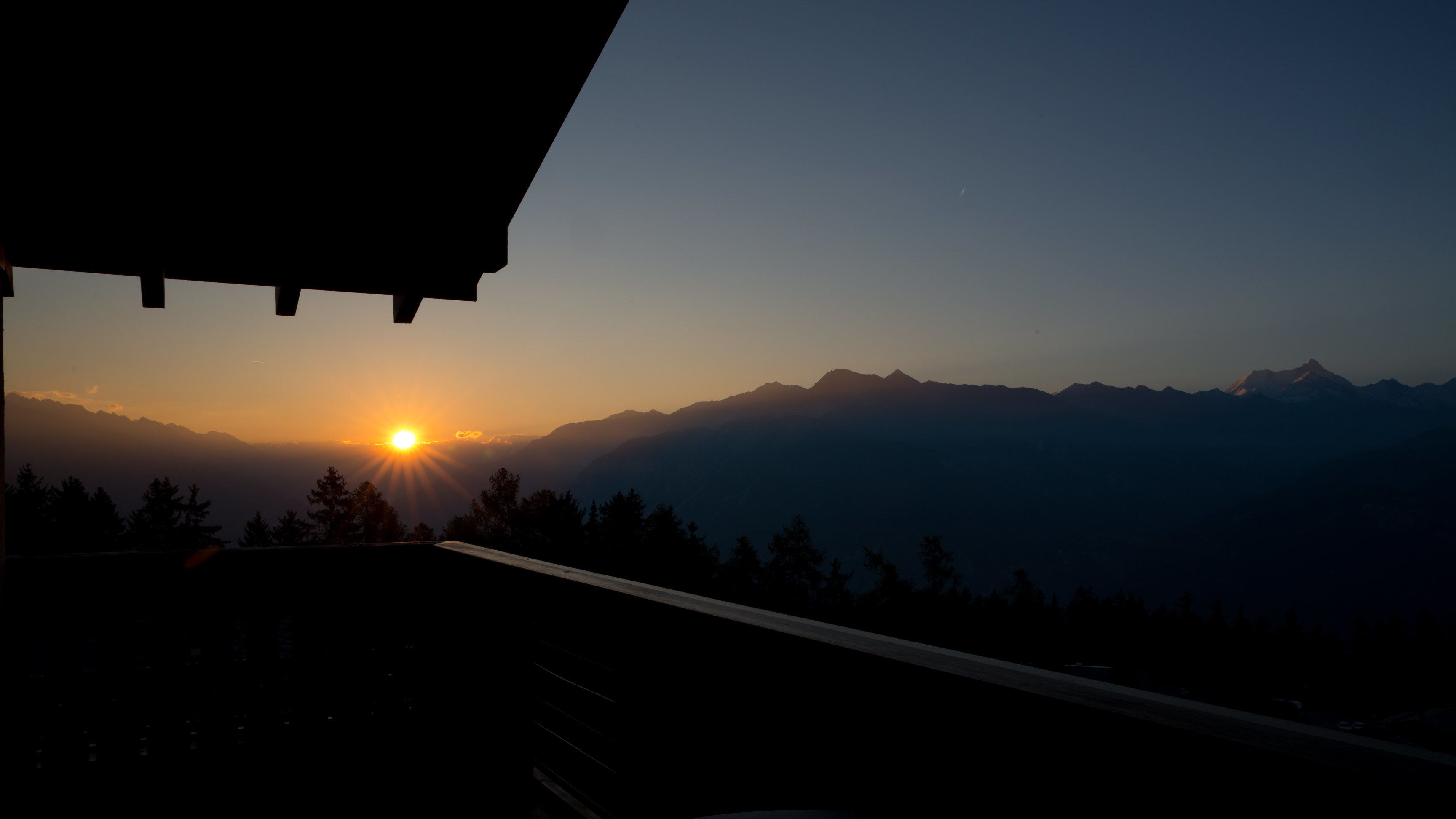 A mountain view with the sun setting behind the peaks.