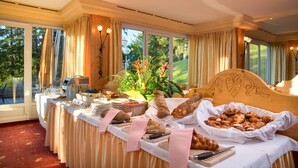 A breakfast buffet with bread, pastries, and a floral centerpiece in a room with large windows and a wooden headboard. - Hotel Helvetia Intergolf (Crans-Montana)