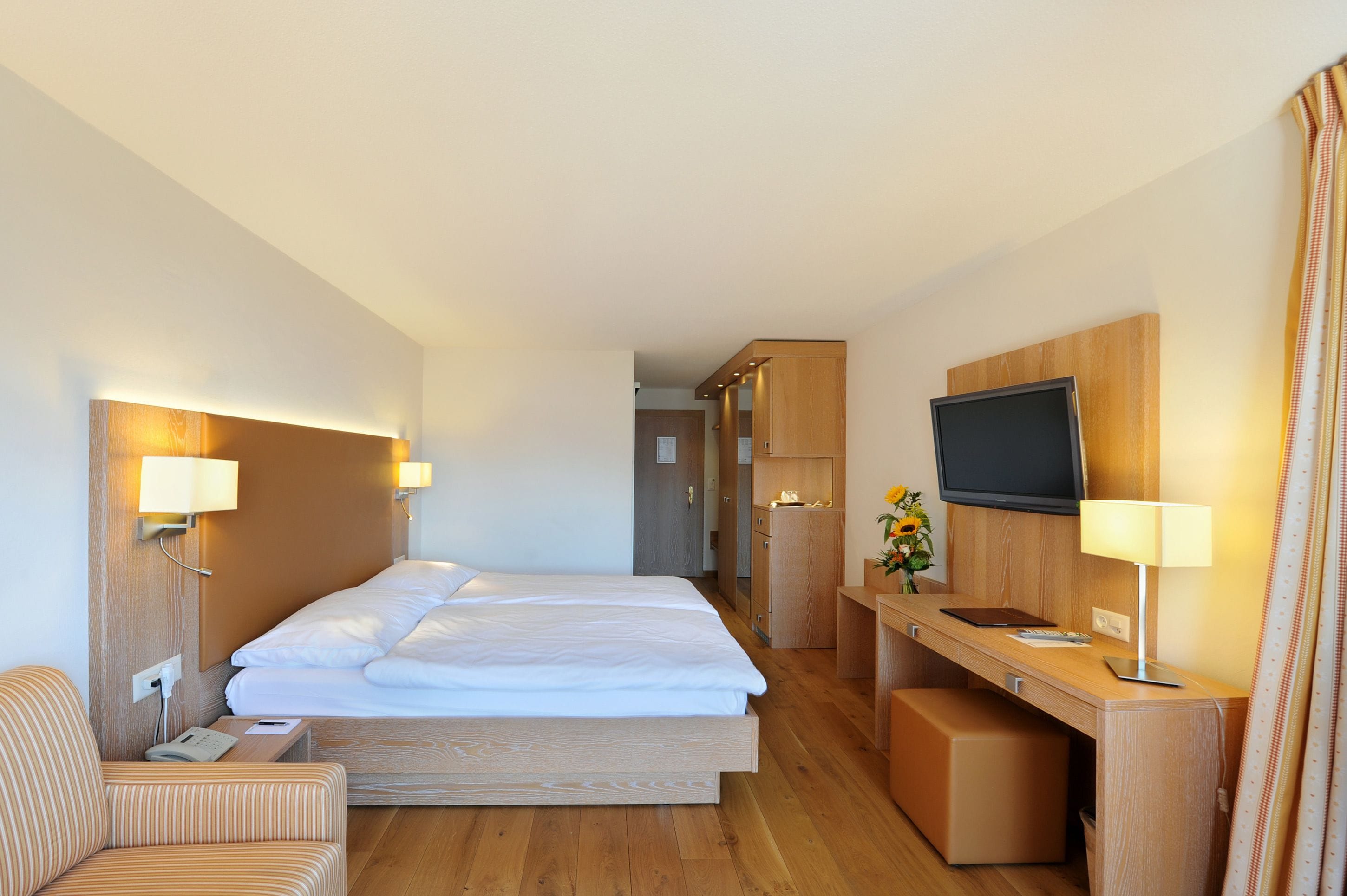 Habitación de hotel con una cama grande, un escritorio con lámpara, televisor y una pequeña zona de estar.