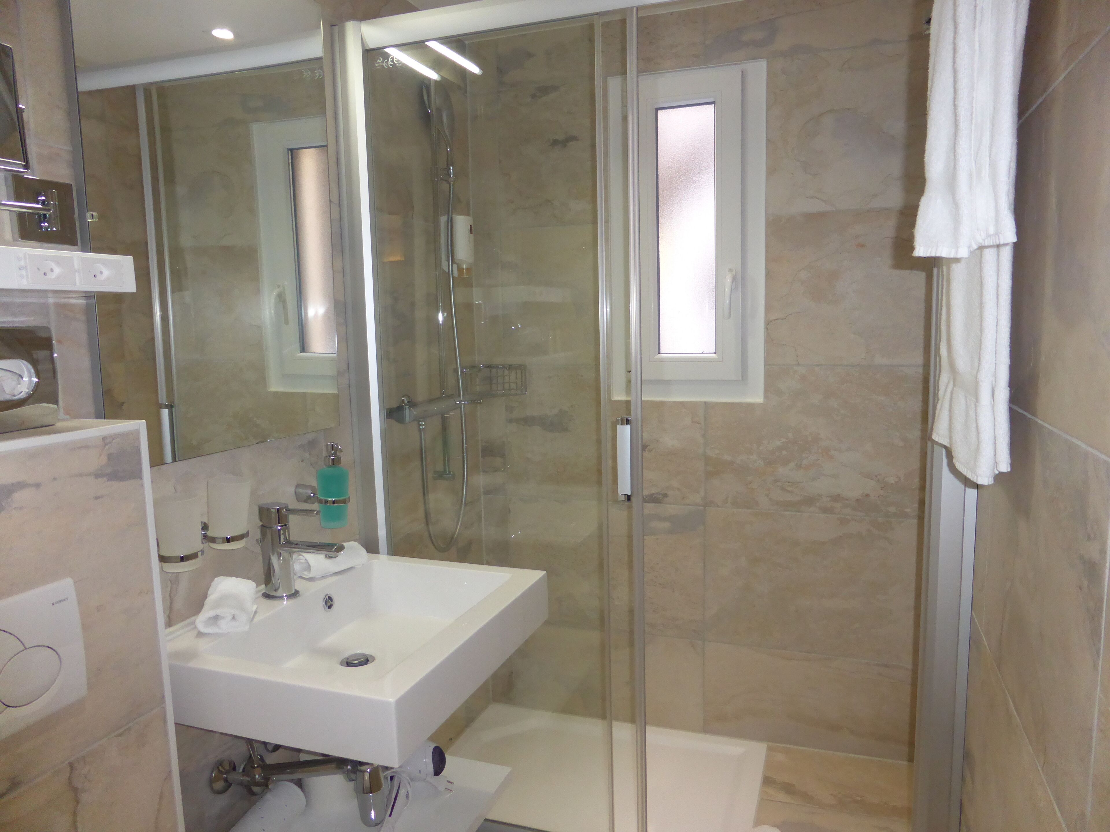 Un baño moderno con ducha de vidrio, un lavamanos blanco y un espejo.