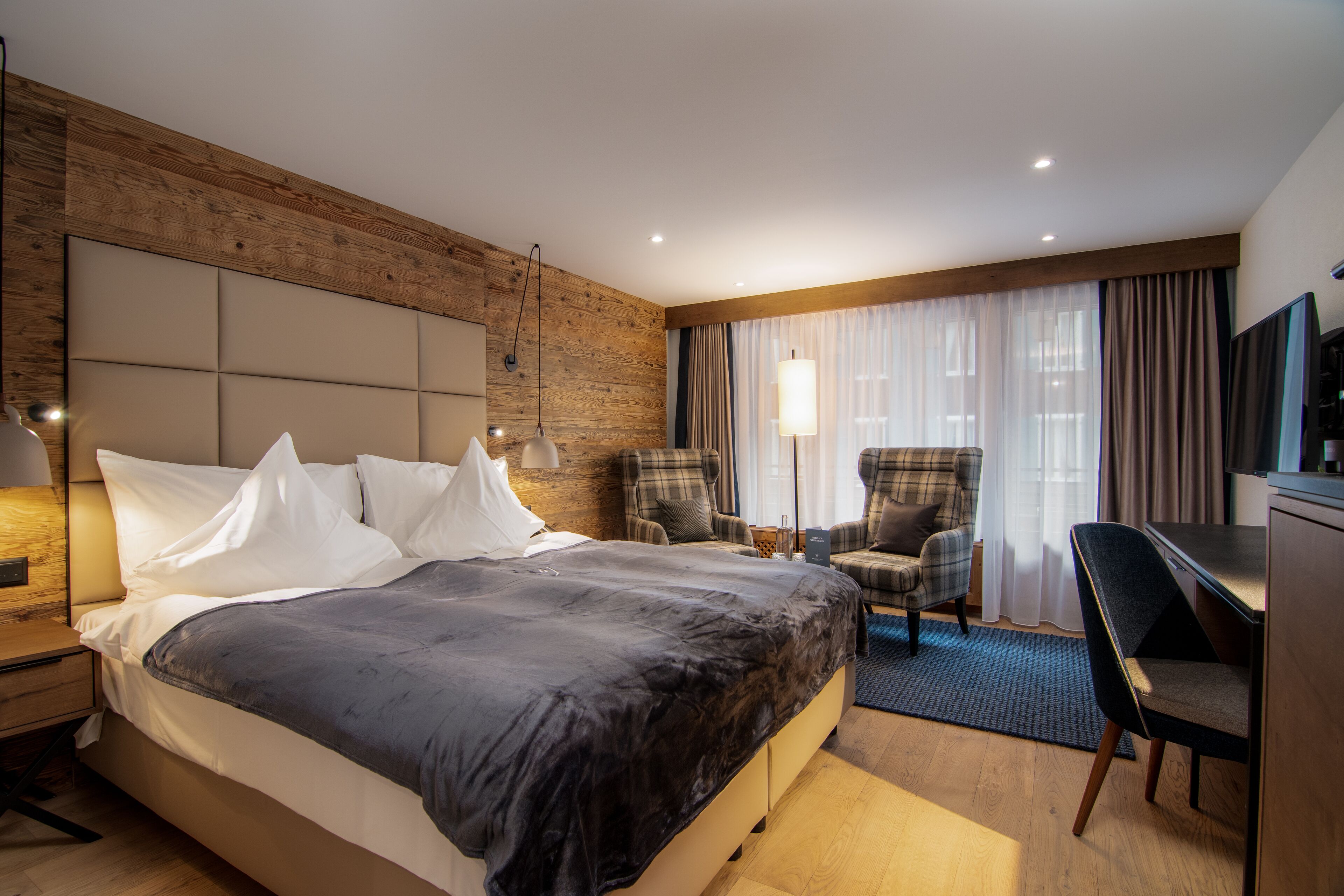 Una habitación de hotel moderna con una cama grande, dos sillones, un escritorio y una televisión.