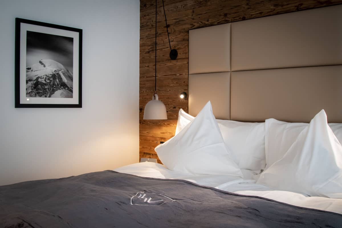 A modern bedroom with a wooden headboard, a framed photograph on the wall, and a bedside lamp.