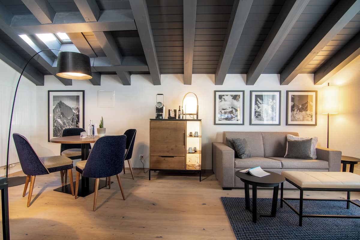 A modern living room with a sofa, coffee table, and chairs. There is a wooden cabinet with shelves and a lamp.