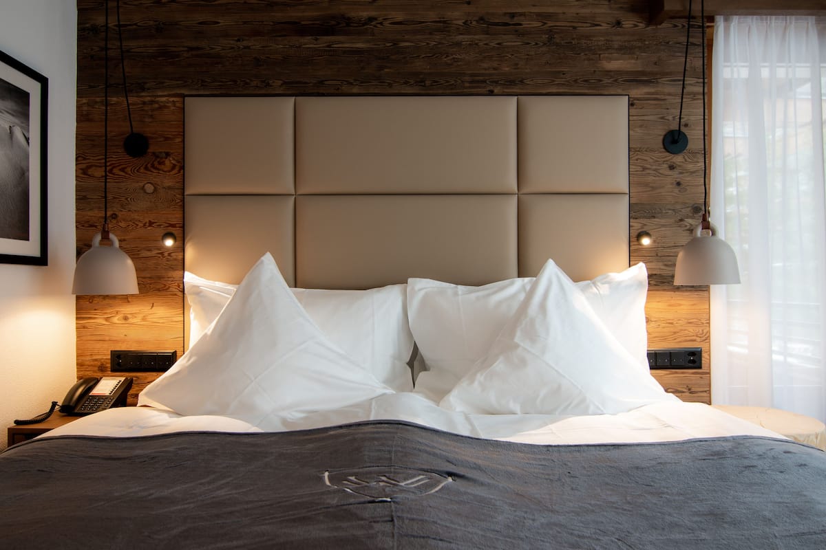 A neatly made bed with a padded headboard, a bedside telephone, and pendant lights.