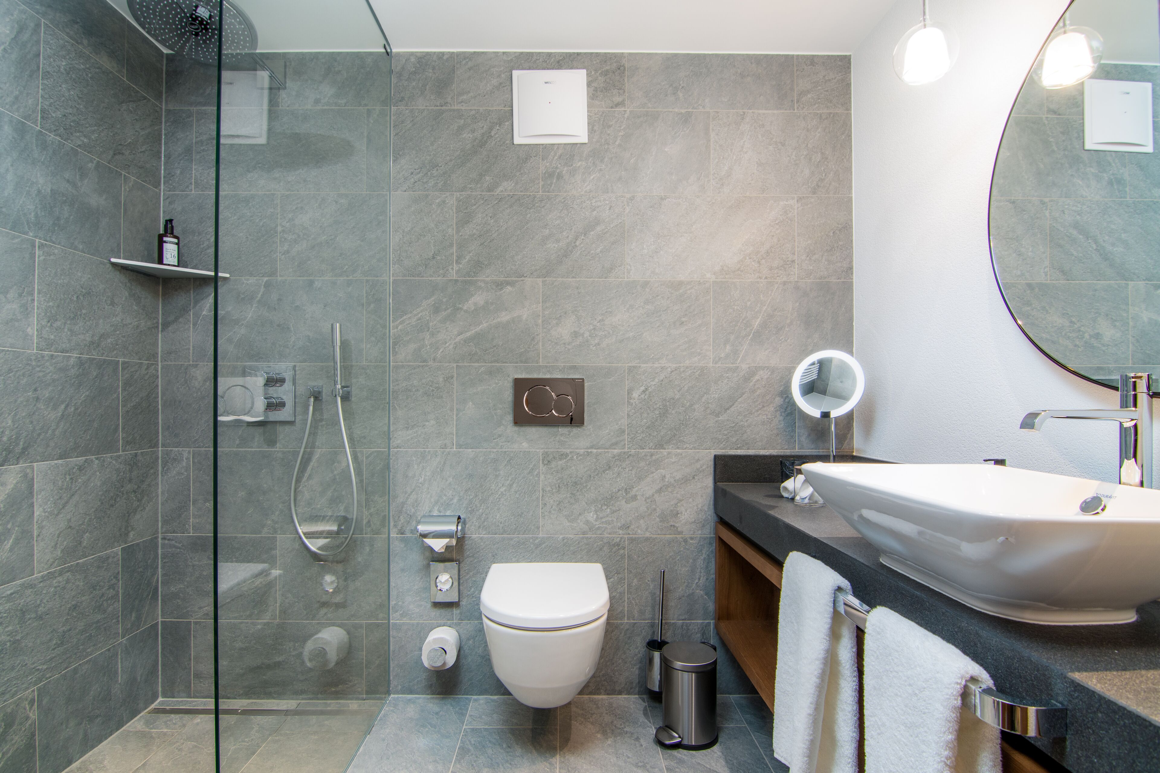 Ein modernes Badezimmer mit Duschkabine aus Glas, einer weißen Toilette, einem Waschbecken mit Spiegel und einem Handtuchhalter.