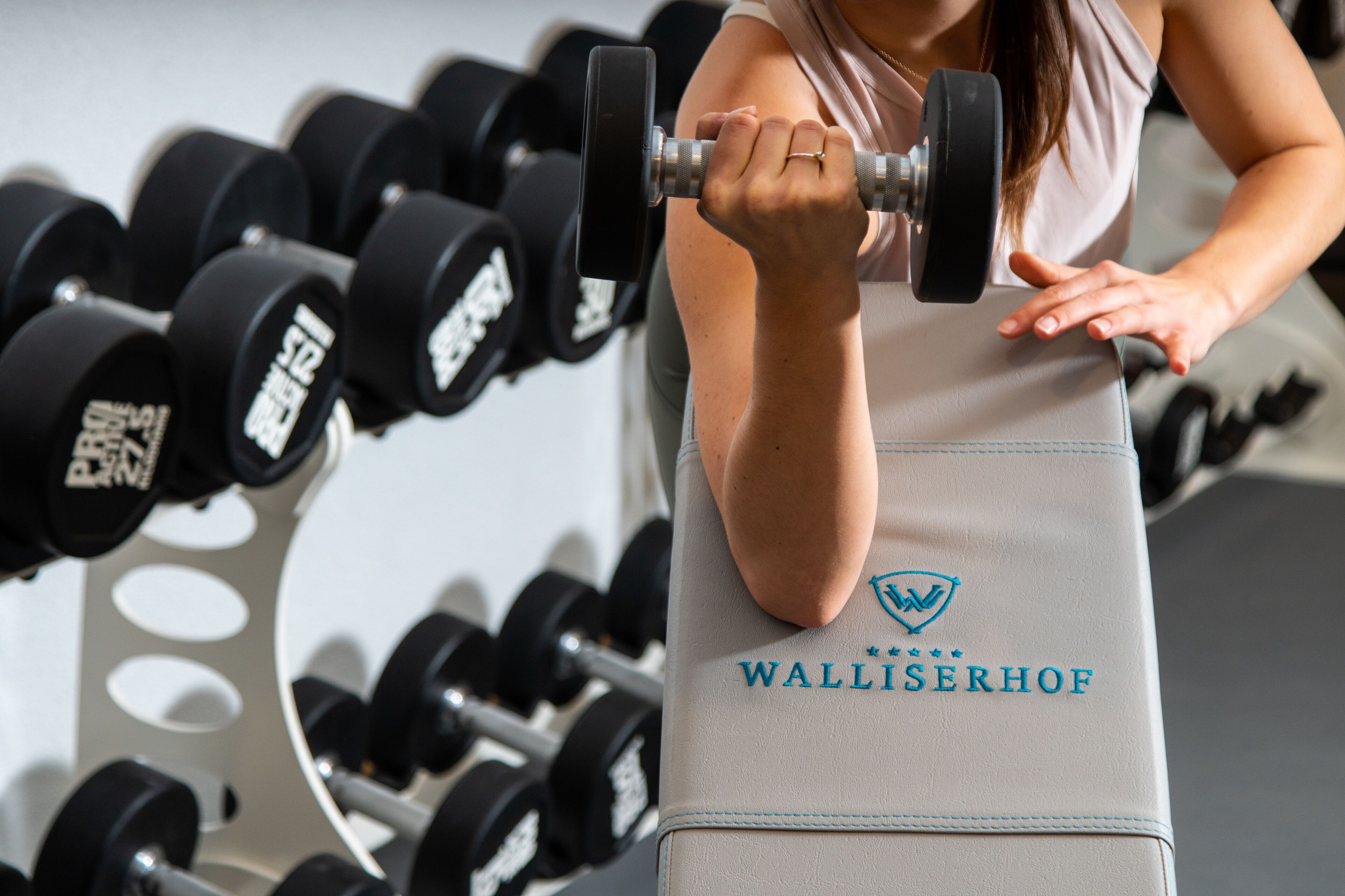 Una palestra con una panca con la scritta "WALLISERHOF" e un rastrello per manubri.