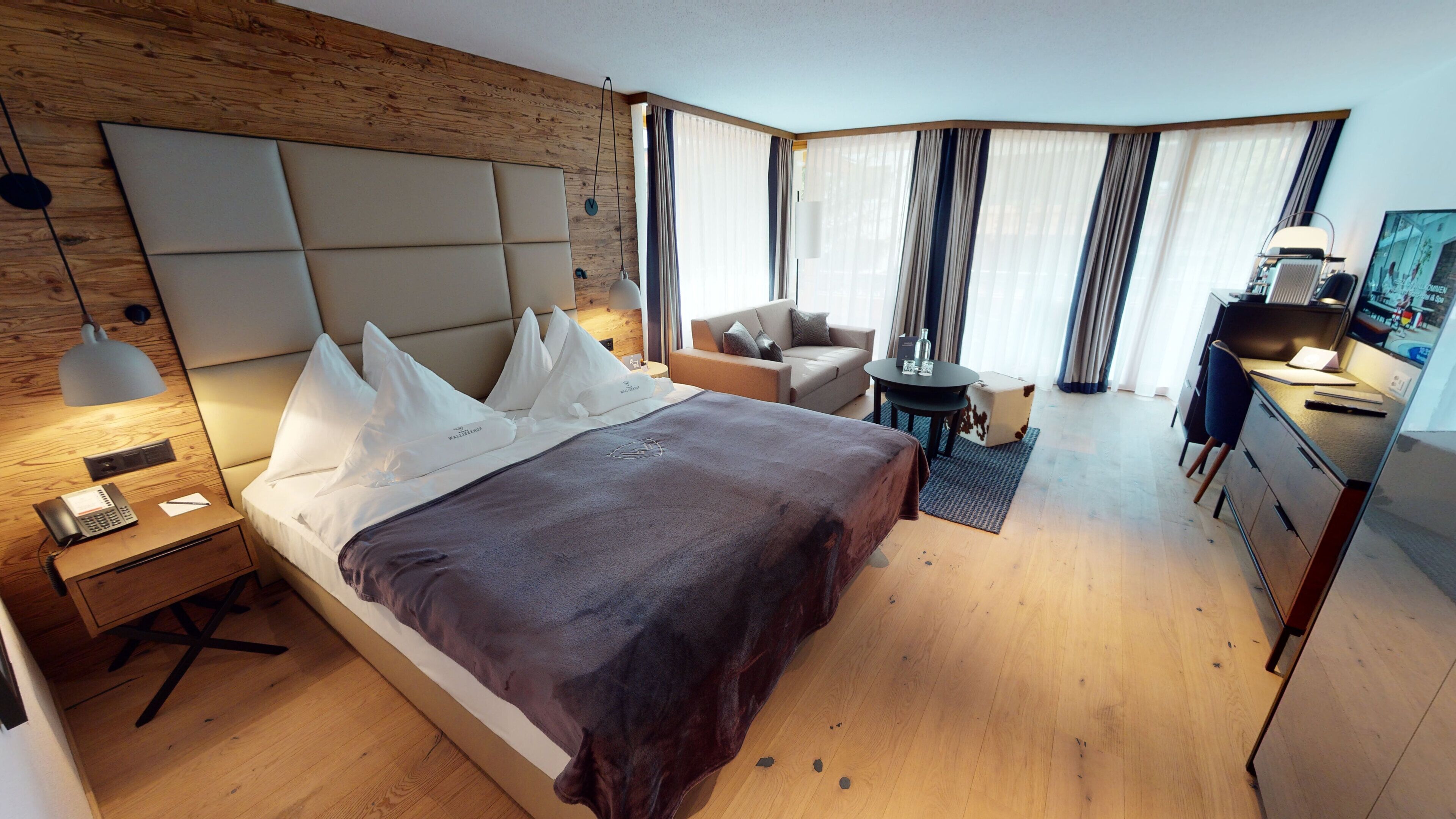 Una habitación de hotel moderna con una cama grande, mesita de noche, lámpara, escritorio, silla y una pequeña mesa con una lámpara.