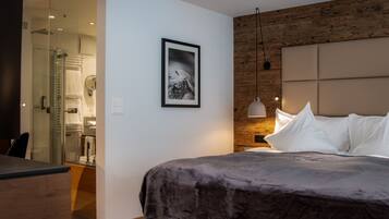 Een moderne slaapkamer met een groot bed, een houten hoofdbord, een ingelijste foto aan de muur en een douchecabine met glazen wanden.