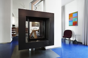 Un interior moderno con una chimenea negra, un sillón rojo y un cuadro abstracto y colorido en la pared.