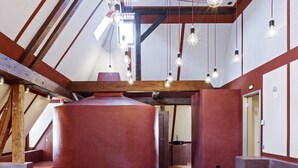 Un'ampia stanza con soffitto a falde, travi in legno a vista e una grande cisterna cilindrica.