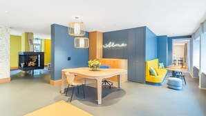 Una hall d'albergo moderna con un tavolo da pranzo in legno, un neon e un divano giallo.