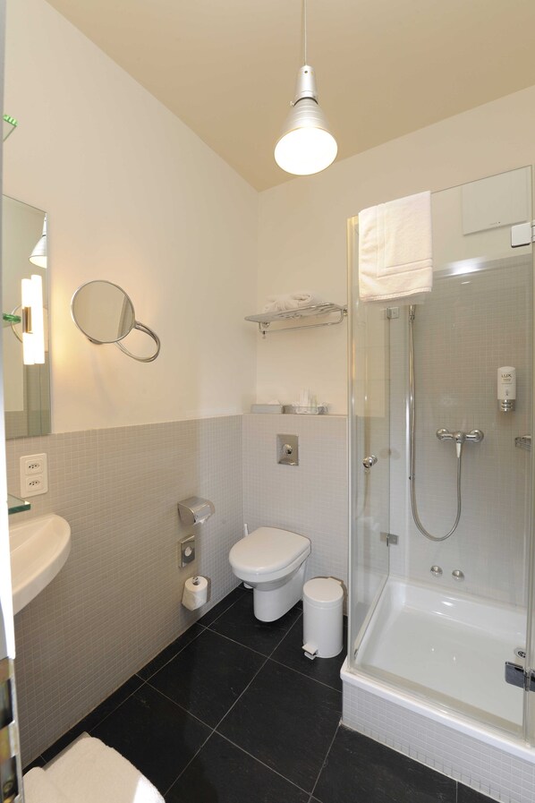 A modern bathroom with a glass-enclosed shower, a white sink, a toilet, and a mirror. - Alma Hotel - Boutique hideaway by the lake with rooftop and ladies-only wellness (Zürich)