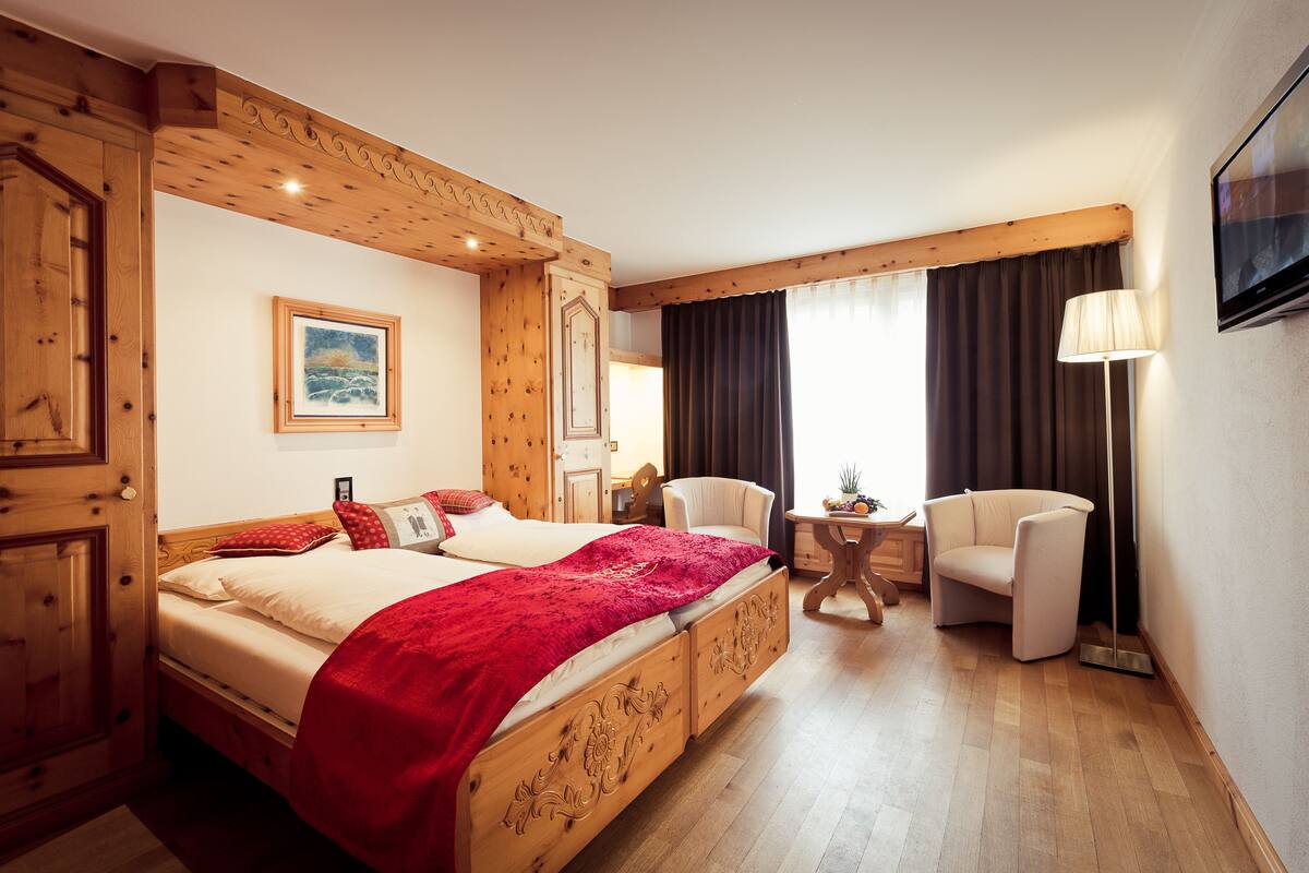 A hotel room with a wooden bed, a chair, a TV, and a painting on the wall.
